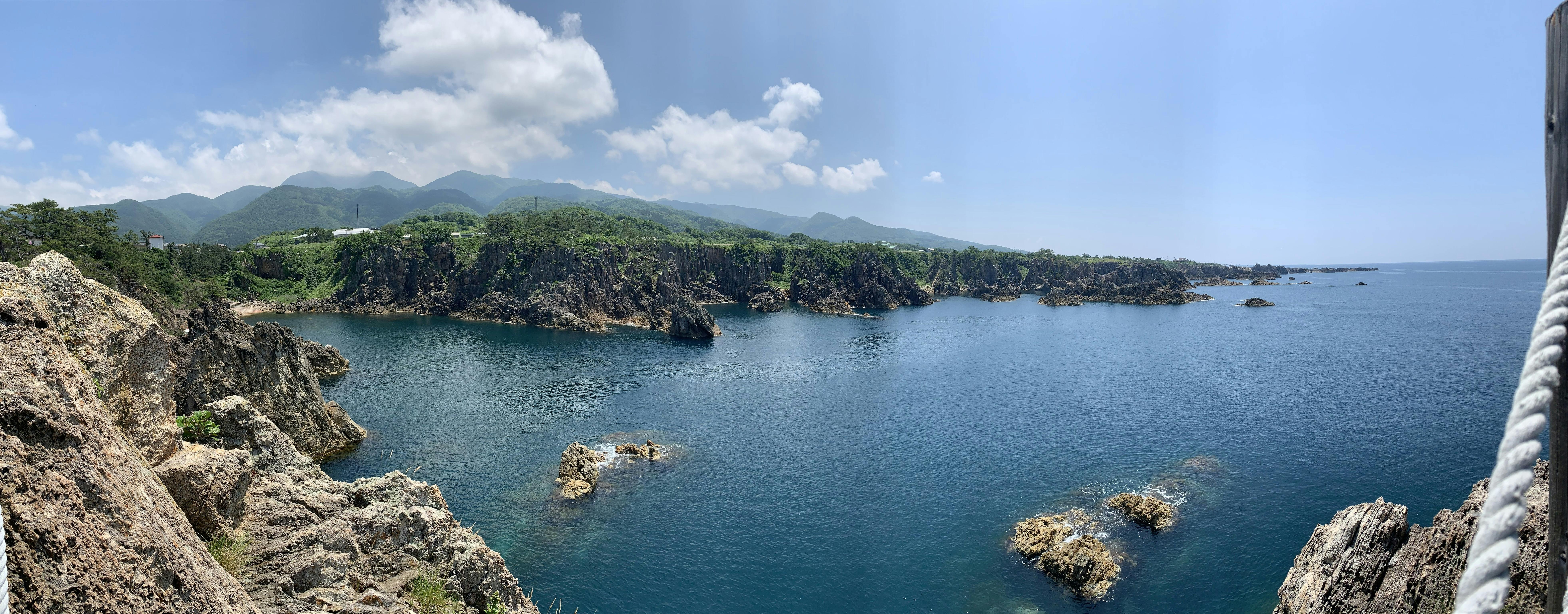 尖閣湾の海と海岸線の岩肌、遠くに見える山々の写真