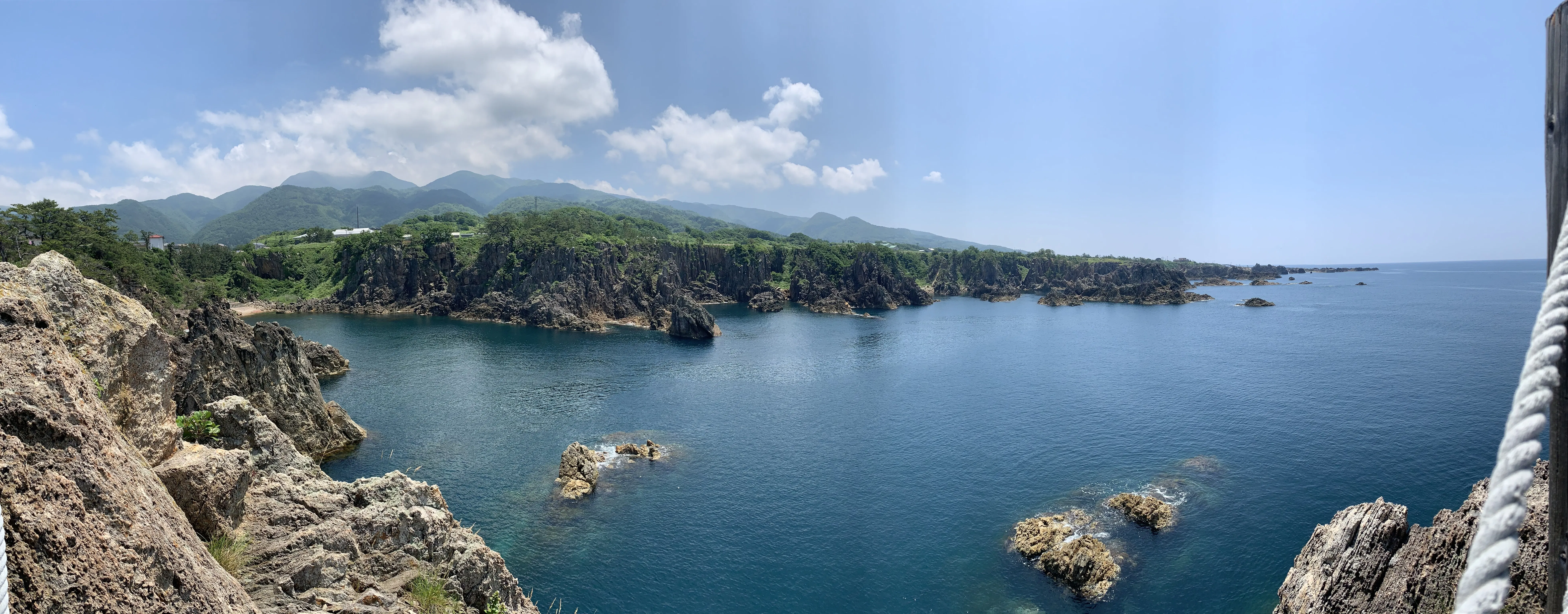 尖閣湾の海と海岸線の岩肌、遠くに見える山々の写真