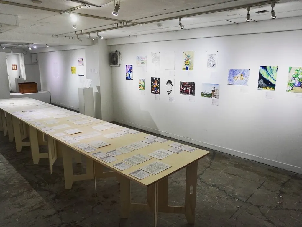 第1回刑務所アート展の展示会場。テーブルにエッセイや詩などの投稿作品、壁面に絵画作品を飾っている