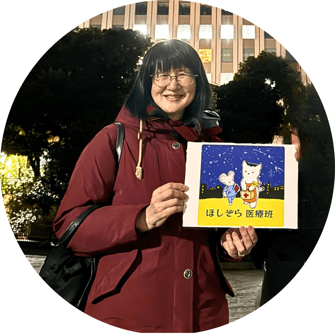 ボランティアスタッフの武田裕子さん（医師、大学教員）の写真。医療相談会の会場で撮影。「ほしぞら医療班」のロゴを手に持って写っている。