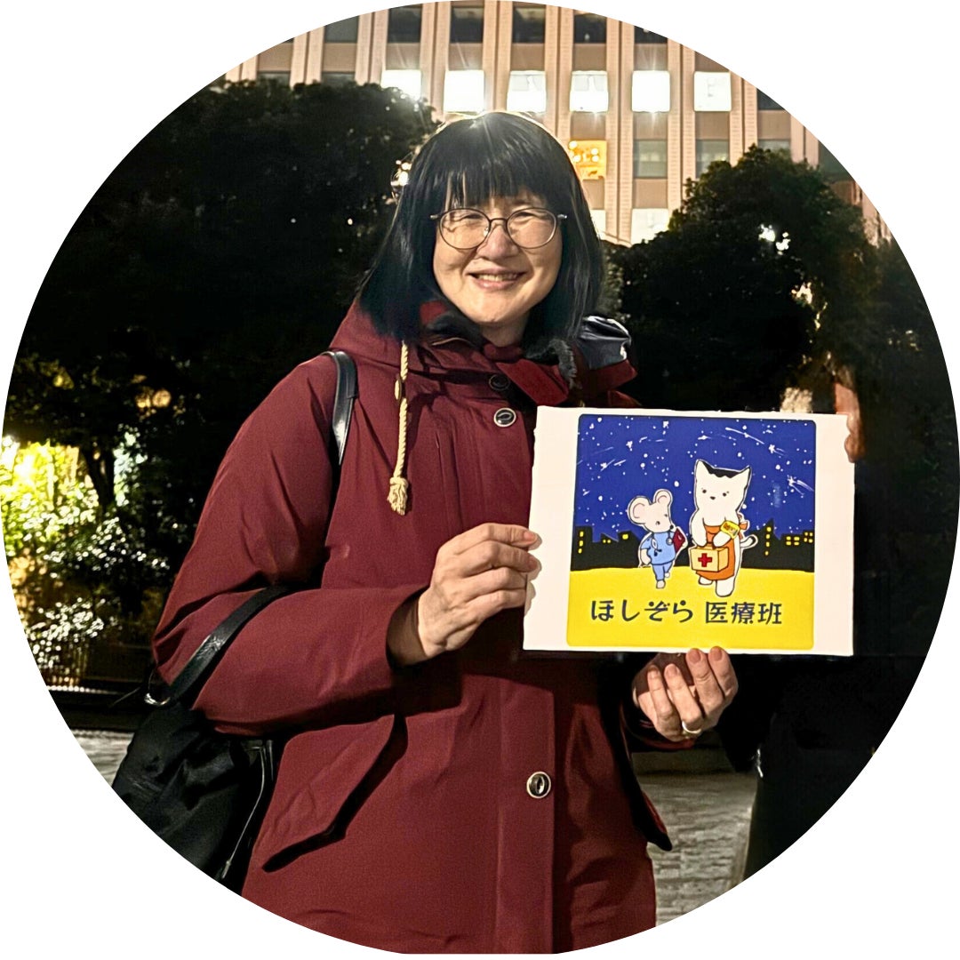ボランティアスタッフの武田裕子さん（医師、大学教員）の写真。医療相談会の会場で撮影。「ほしぞら医療班」のロゴを手に持って写っている。
