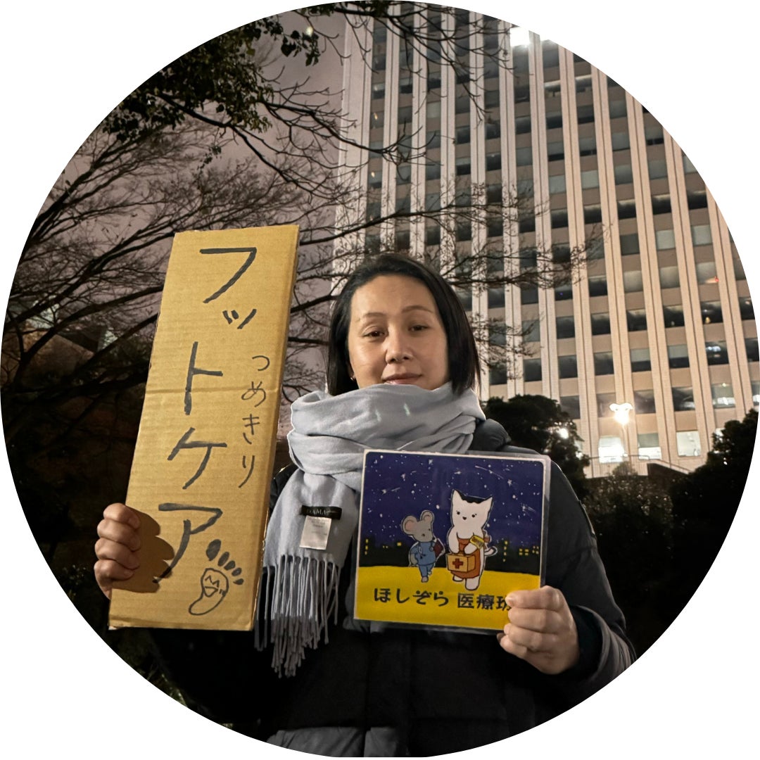 ボランティア看護師の伊奈ちとせさんの写真。左手に「ほしぞら医療班」のロゴ、右手に「フットケア」と記載された看板を持っている。