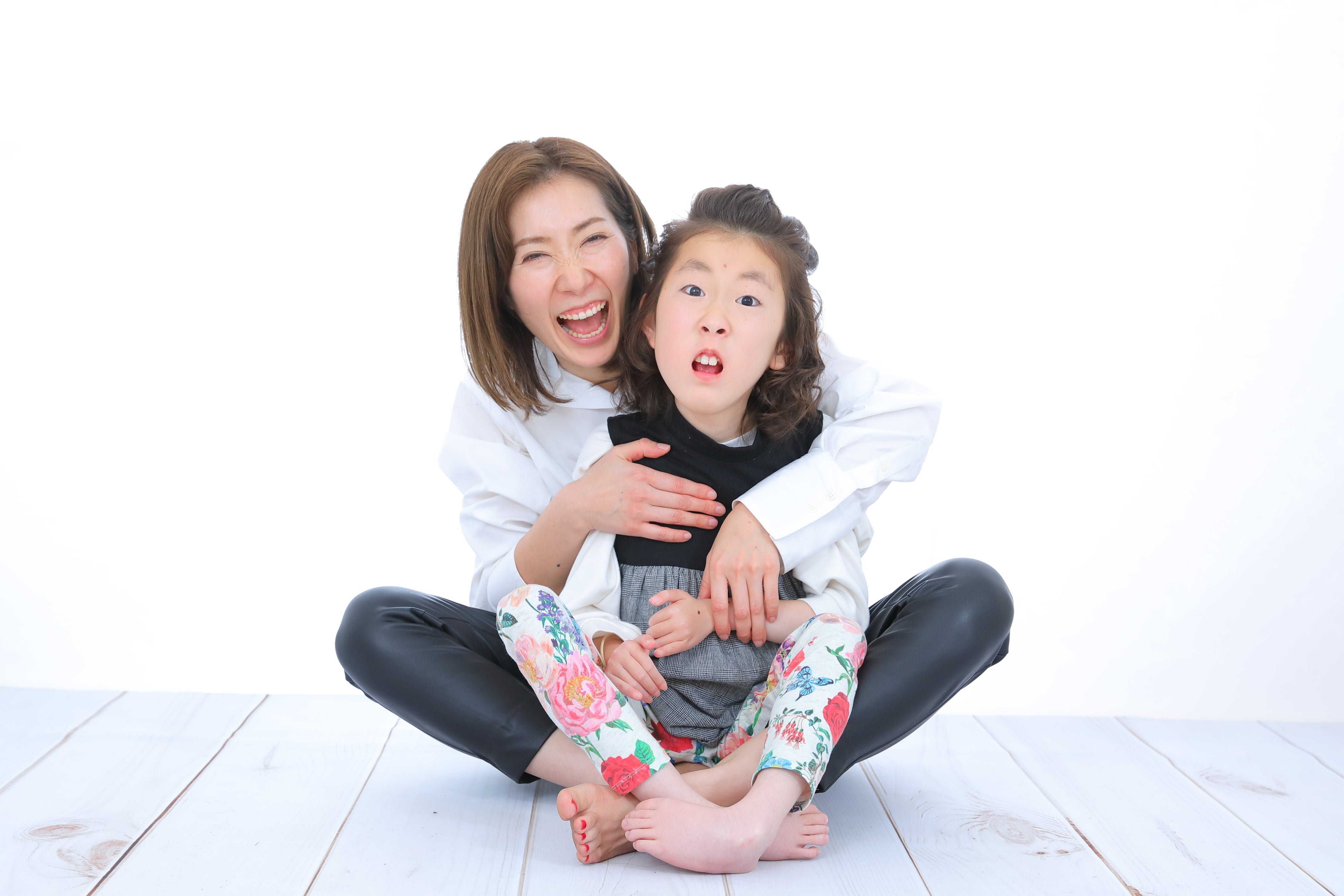 大きな口を開けて笑う母さくらがあぐらをかいた上に座る娘のマコ