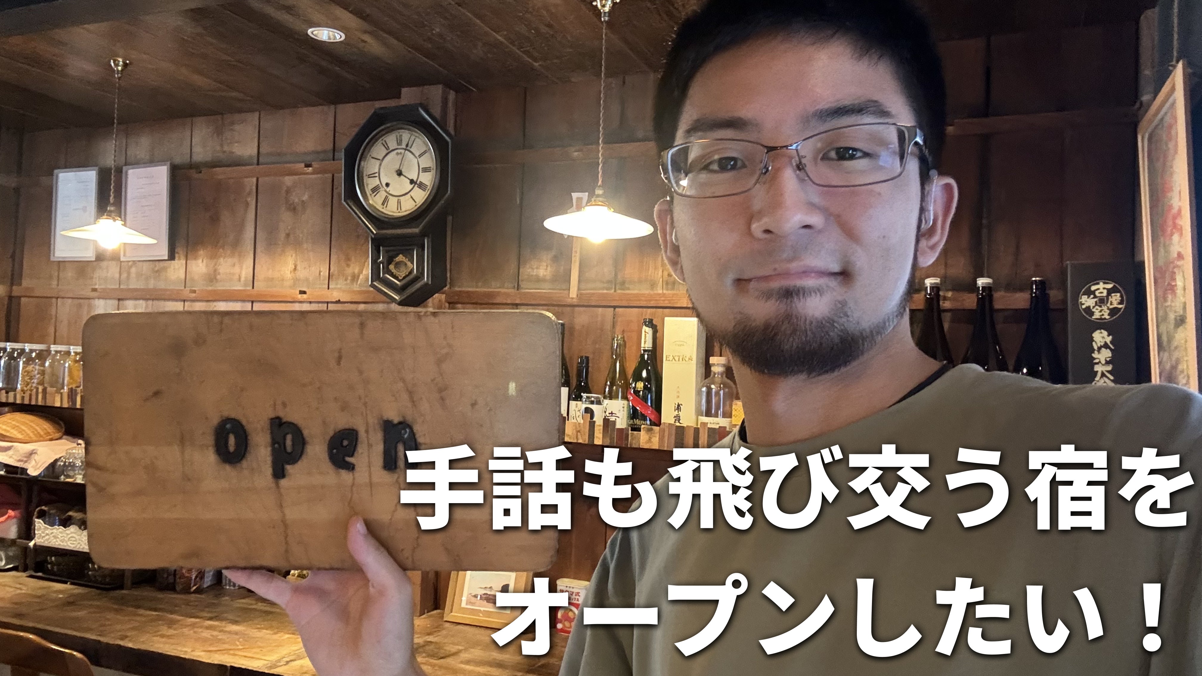 古民家ながらもオシャレな空間のヤマイロゲストハウスでにて竹花がopenと書かれた看板を手にしている様子を背景に、白文字で「手話も飛び交う宿をオープンしたい！」