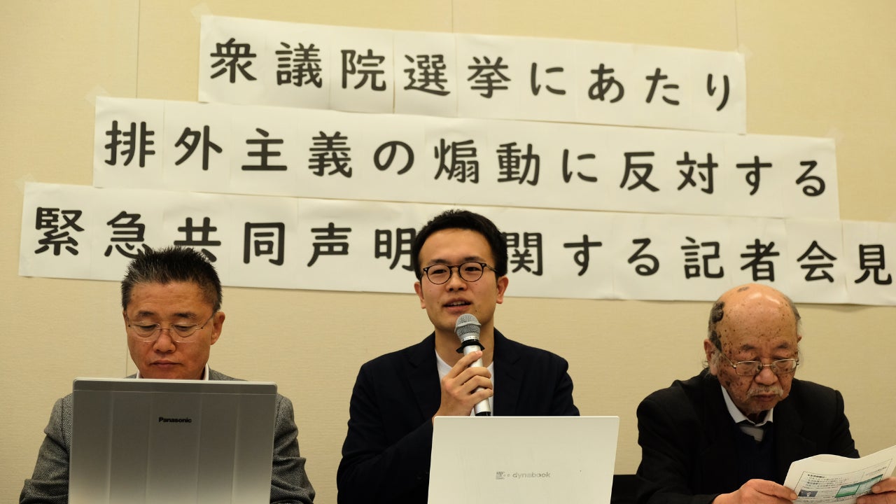 2026年1月26日、衆議院会館にて行われた記者会見の様子。中央には、つくろい東京ファンド事務局長の大澤が座り、マイクを握って真剣な表情で発言しています。  背後の壁には、A4用紙を繋ぎ合わせて作られた大きな横断幕が貼られており、「衆議院選挙にあたり 排外主義の煽動に反対する 緊急共同声明に関する記者会見」という文字が並んでいます。