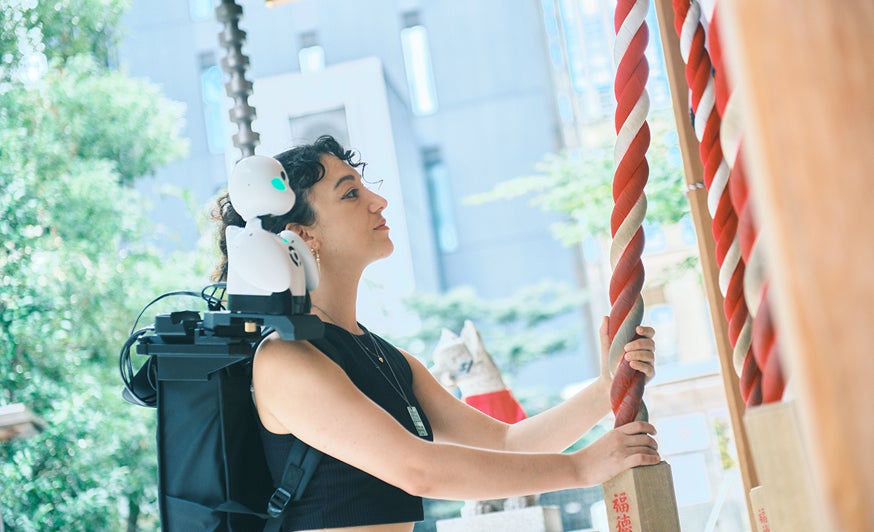 肩に分身ロボットオリヒメをのせて、神社に参拝する女性の写真