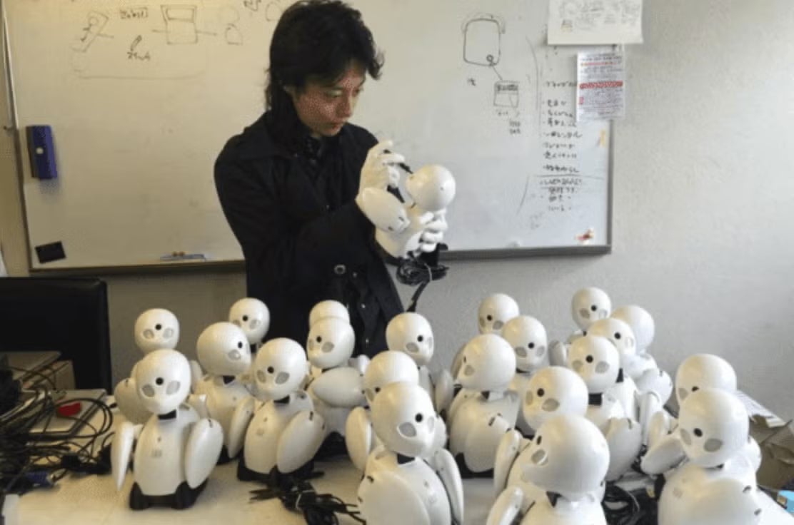OriHimeの開発を始めた頃の吉藤オリィ。中央でOriHimeを組み立てている。机の上には大量のOriHime
