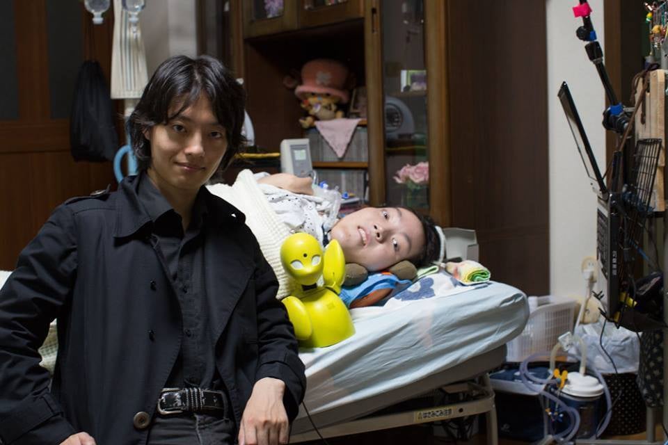 ベッドの上で横たわる番田と、その前にいる吉藤の写真